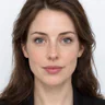 Olivia Maria Colman, with shoulder-length brown hair and a black blazer, facing the camera on a white background